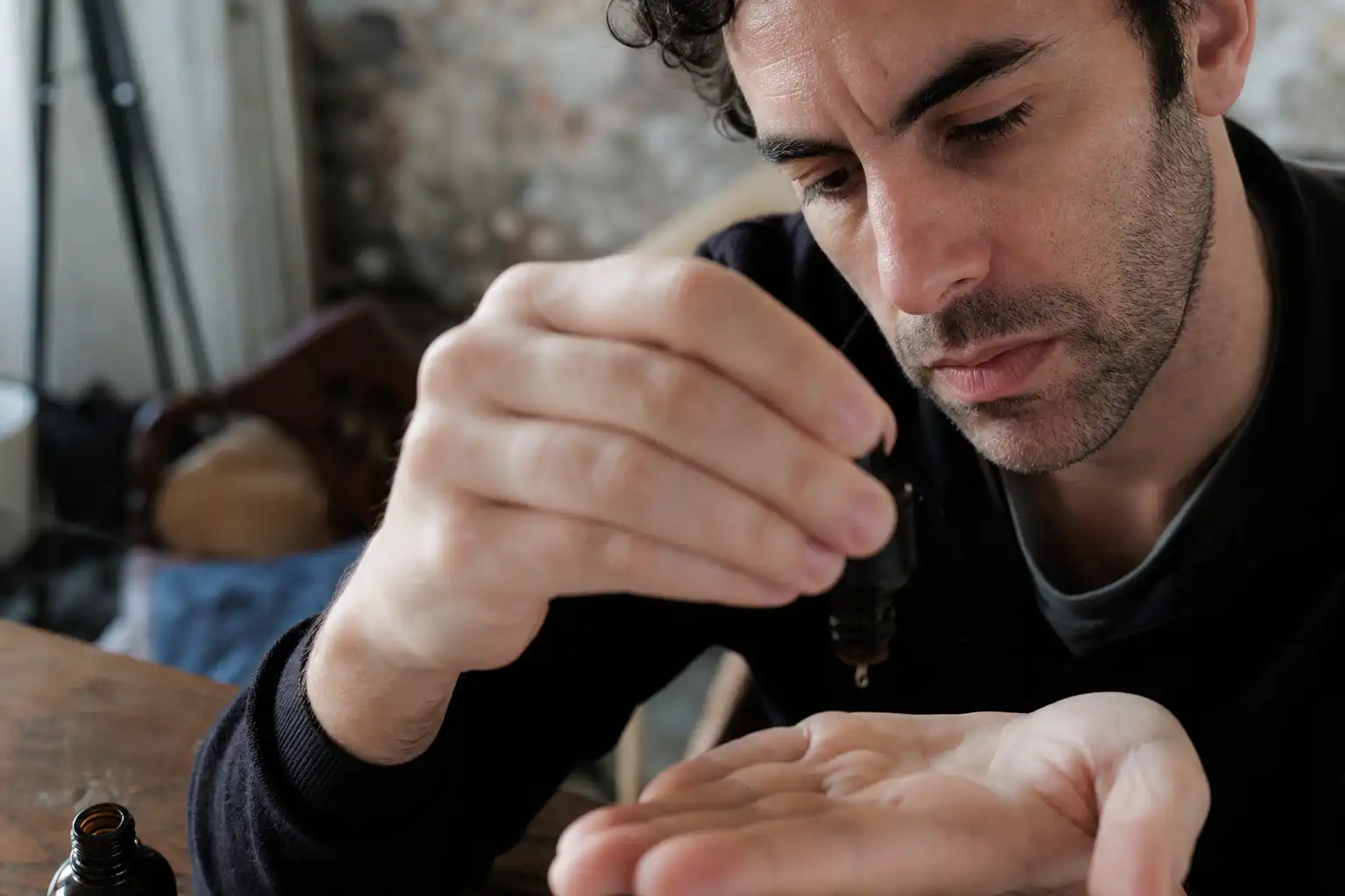 Des mains dosent quelque chose, autour de sacha baron cohen, près d'une table en bois.